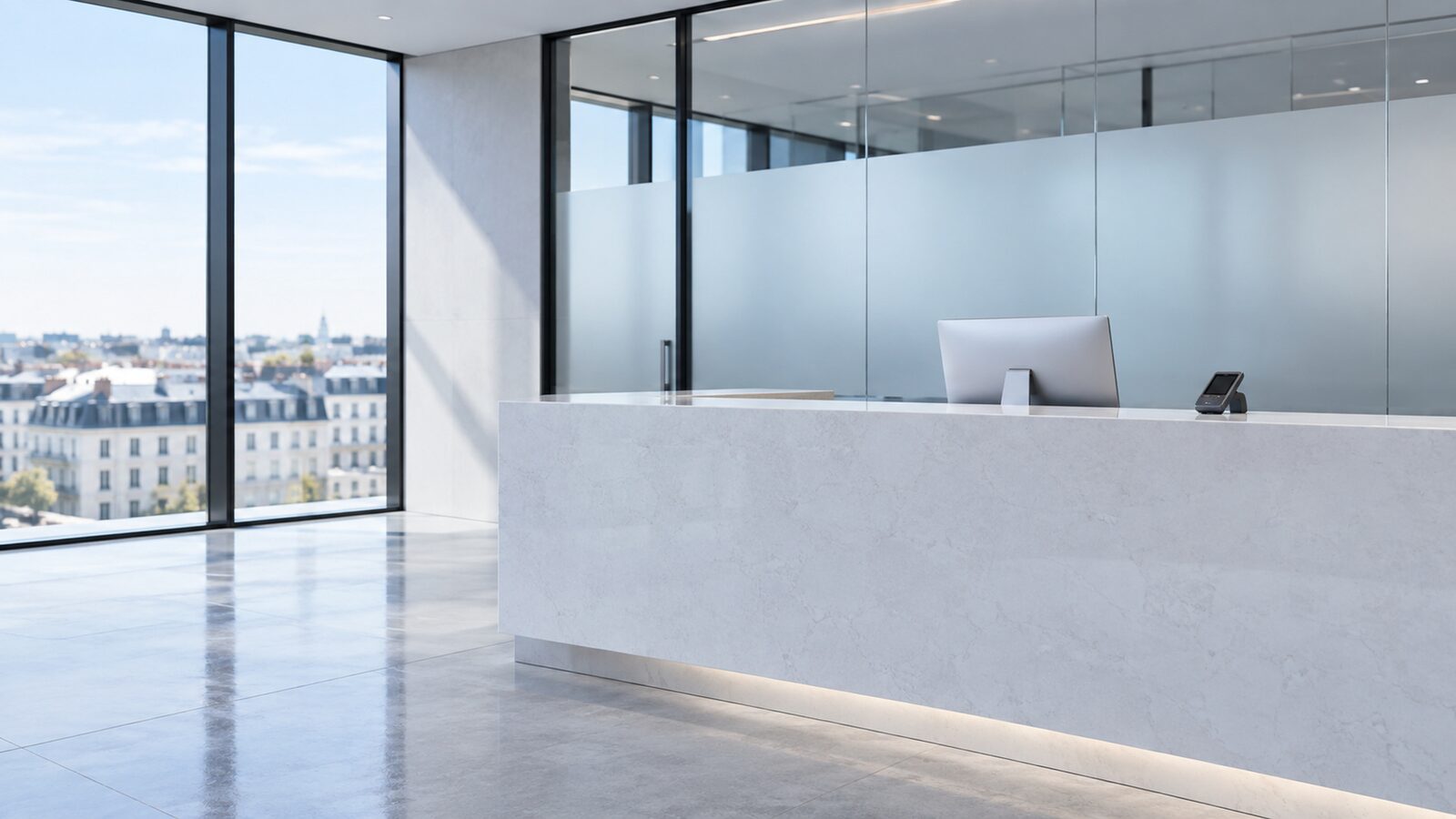 Reception desk in light stone with a monitor in a bright office with a glass front.