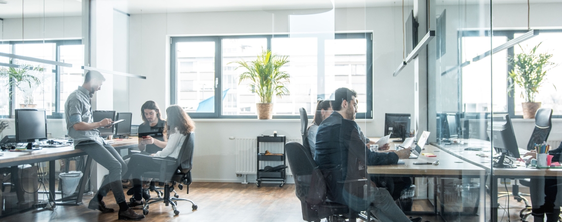 Modern office with employees collaborating on digital devices, representing teamwork and productivity with Microsoft 365 tools.